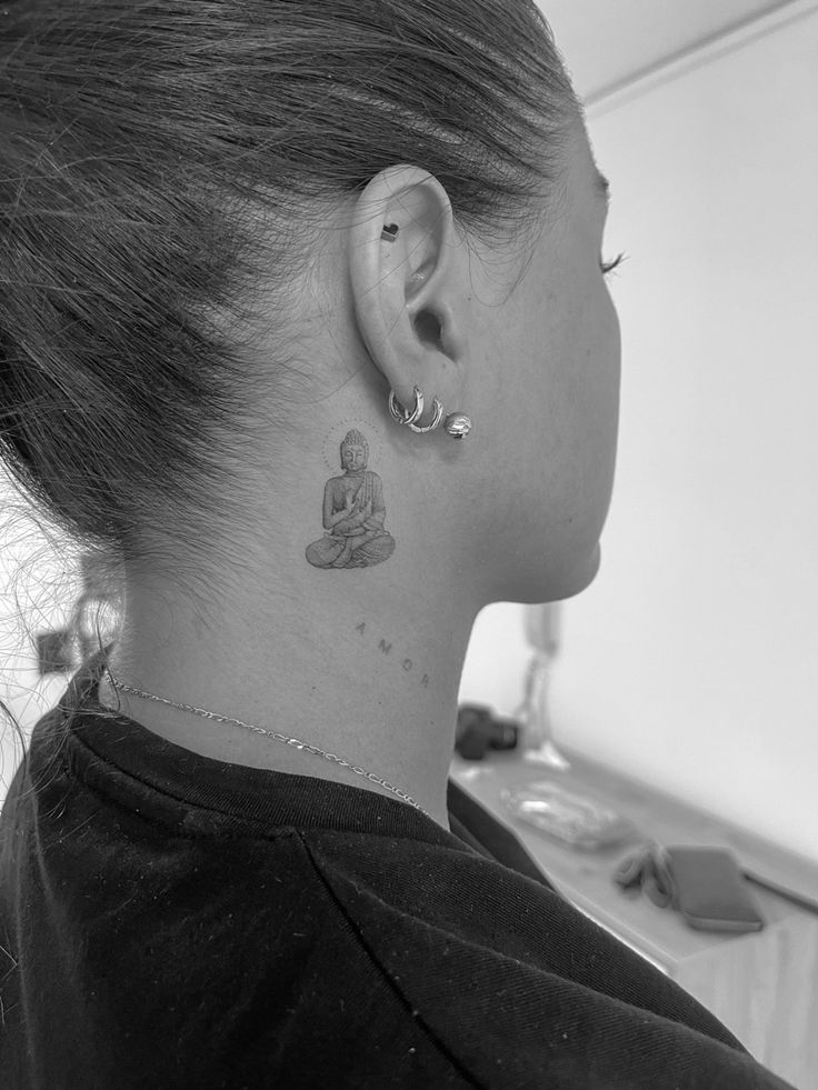 a woman with a small buddha tattoo on her left side of her neck and behind her ear