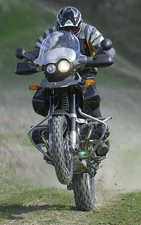 a man riding on the back of a motorcycle down a dirt road next to a lush green field