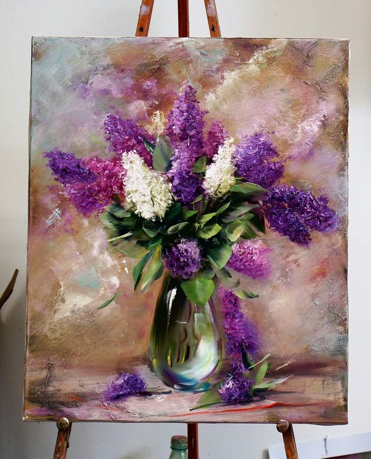 a painting of purple and white flowers in a vase on an easel with paintbrushes