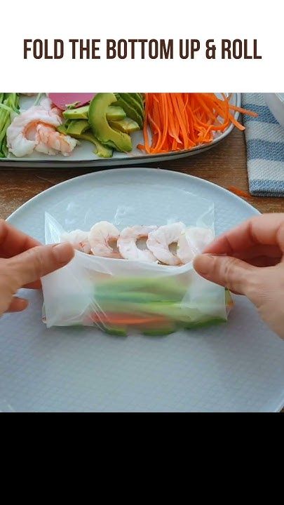 two hands holding up some food on a plate with vegetables and carrots in the background