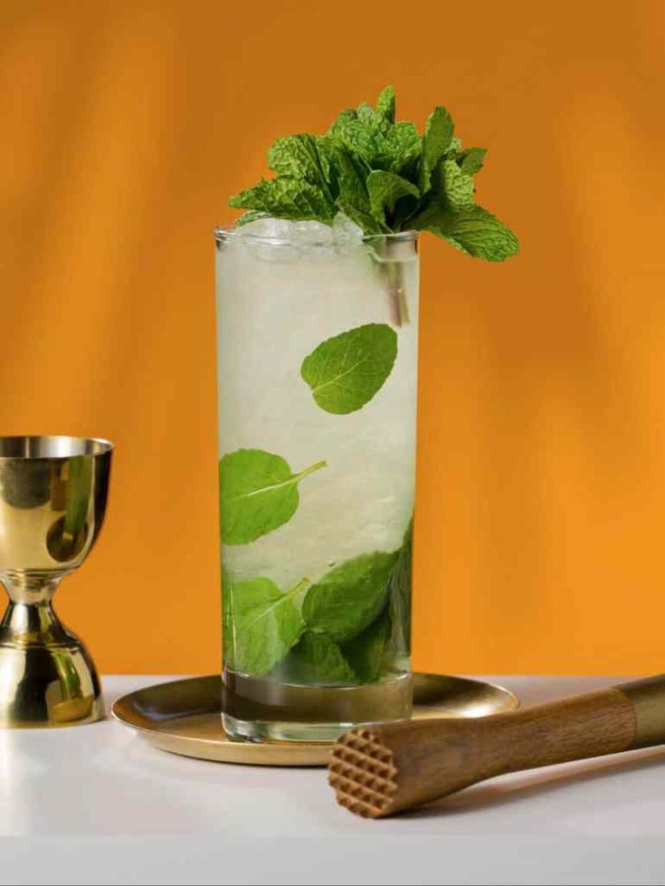 a tall glass filled with ice and mint on top of a table next to a chalice