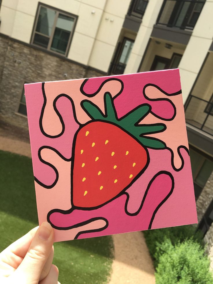 a hand holding up a pink card with a strawberry painted on the front and side