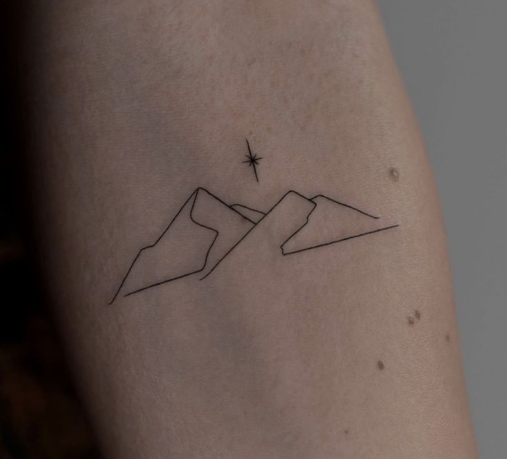 a small tattoo on the back of a woman's left arm, with mountains in the background