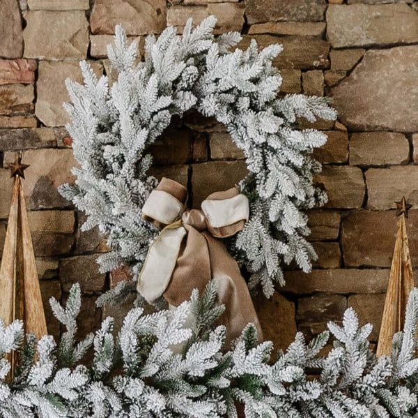 a christmas wreath on a brick wall next to two small trees with white and brown bows