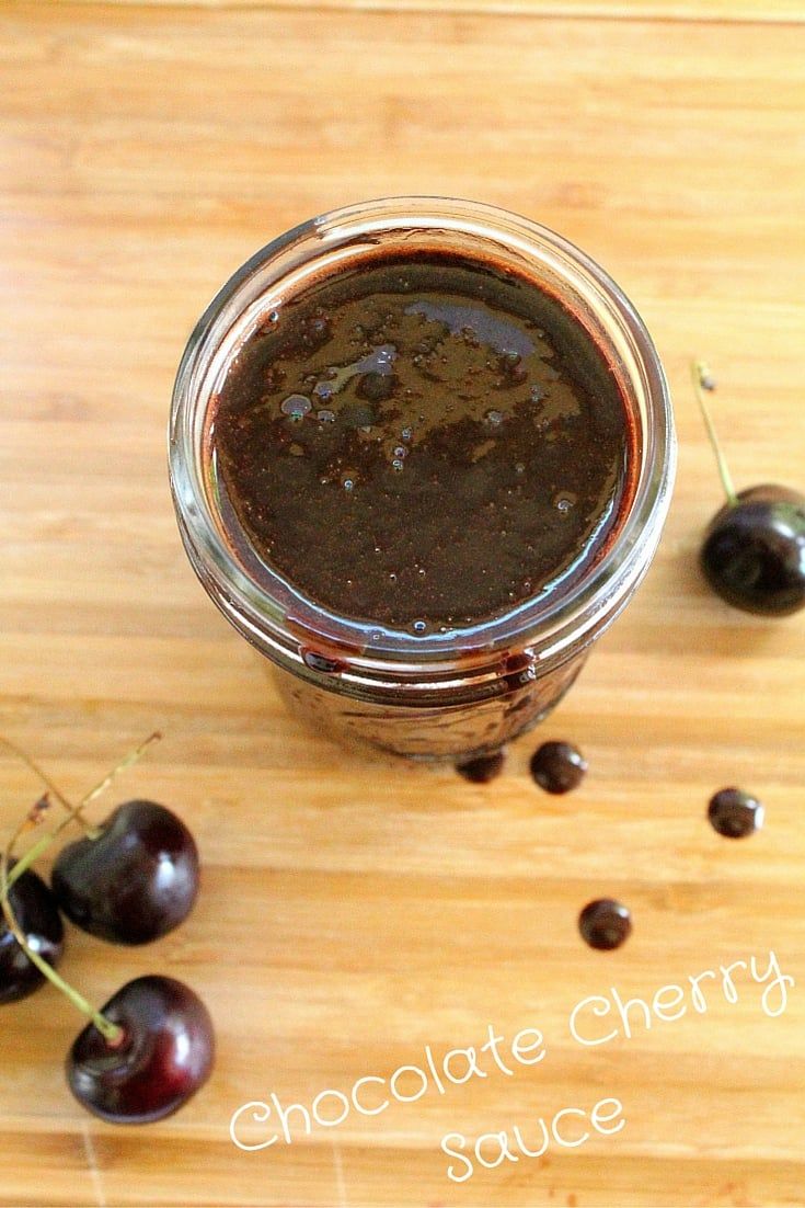 a jar filled with chocolate cherry sauce next to some cherries