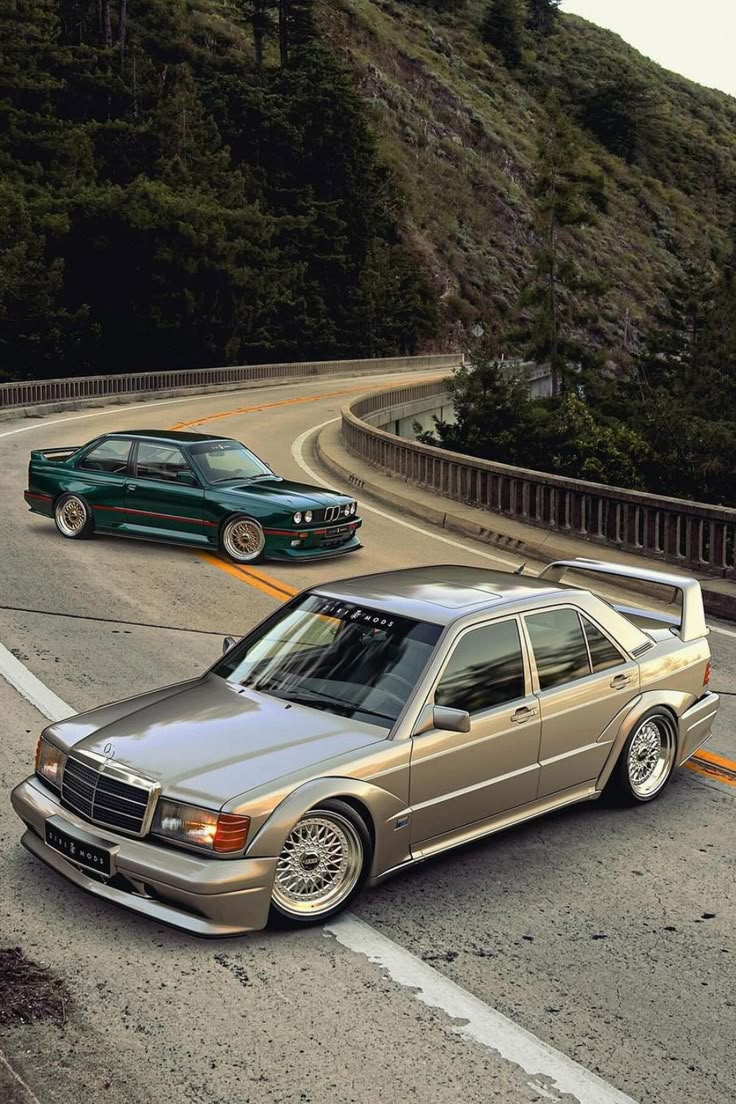 two cars driving down the road next to each other in front of a mountain range