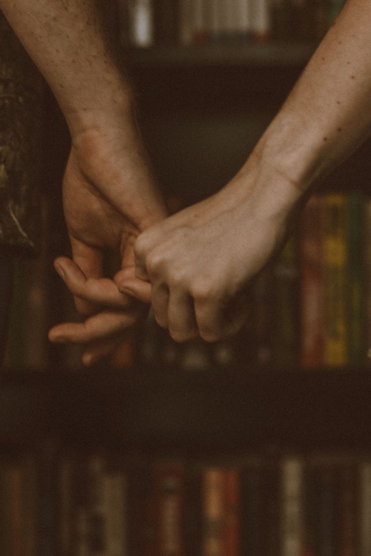 two people holding hands in front of a bookshelf