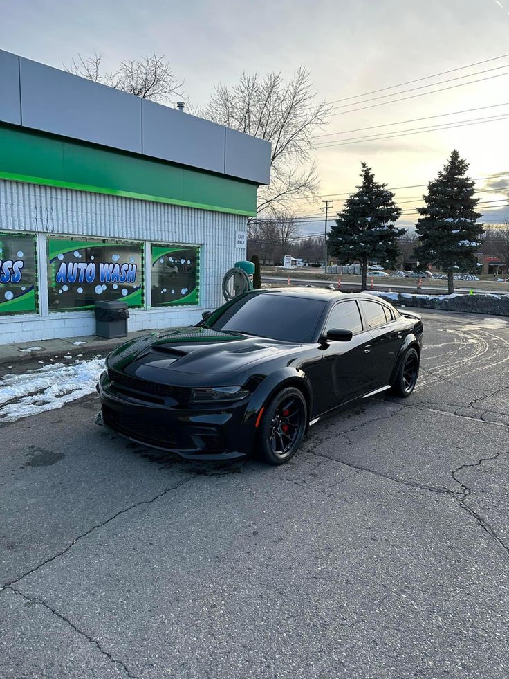 a black car is parked in front of a store with snow on the ground and trees