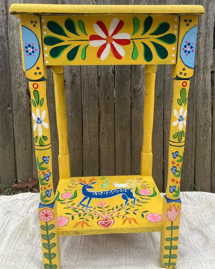 a yellow painted stool with a deer on it's side and flowers around the top