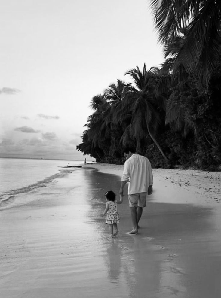 a man and child walking on the beach with palm trees in the backgroud