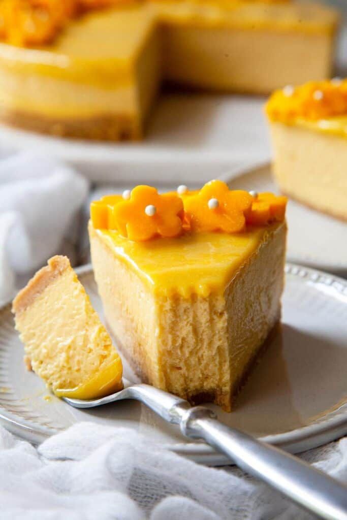 a piece of cheesecake on a plate with a fork next to it and another slice in the background