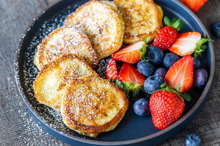 french toast, strawberries and blueberries on a black plate with powdered sugar