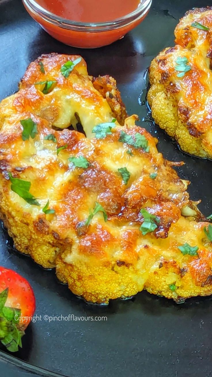 two pieces of fried food on a black plate next to tomatoes and ketchup