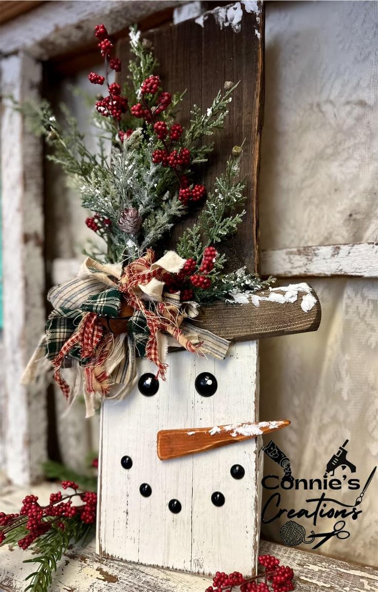 a snowman made out of an old wooden block with red berries and greenery