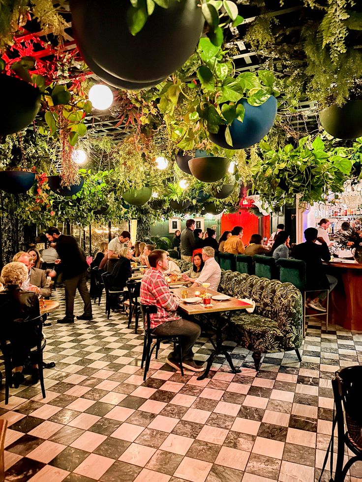 people sitting at tables in a restaurant with plants hanging from the ceiling