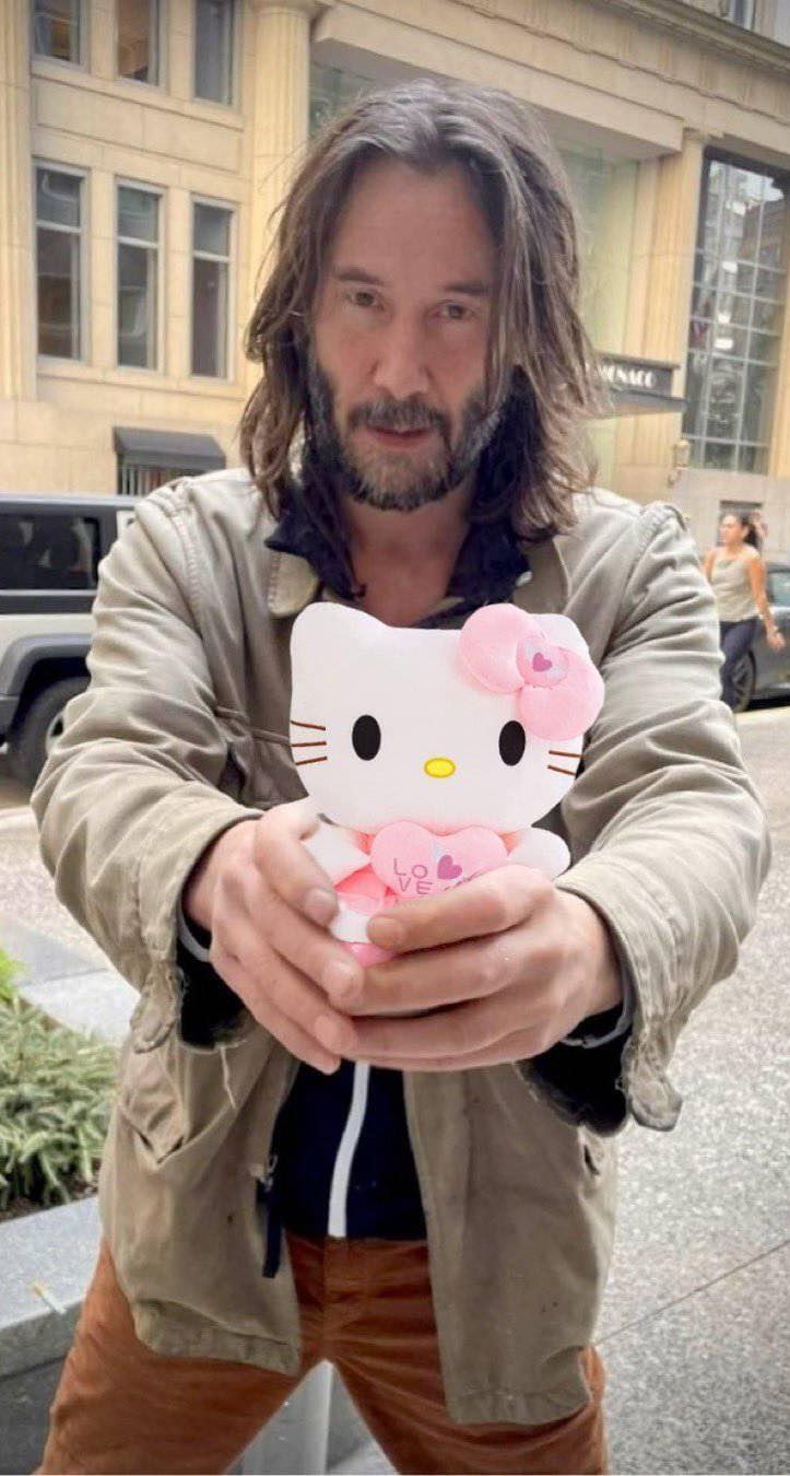 a man with long hair holding a hello kitty doll in front of his face and looking at the camera