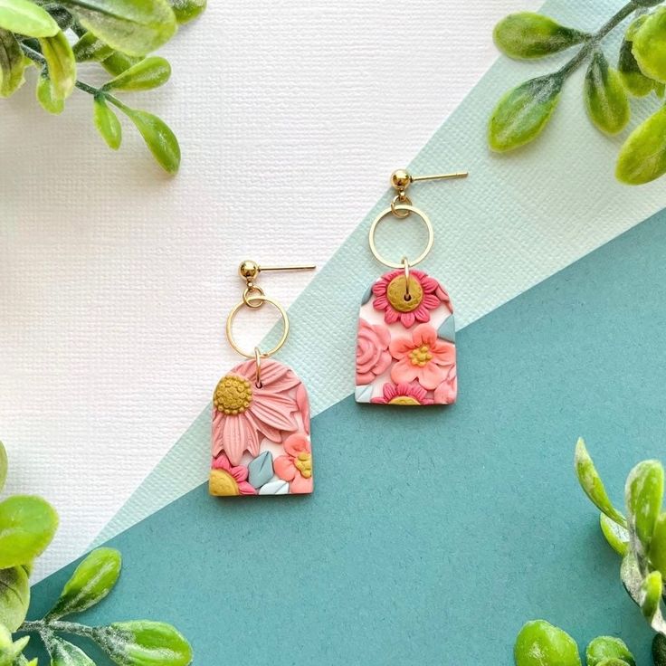 two pink flowers are hanging from earrings on a blue and white background