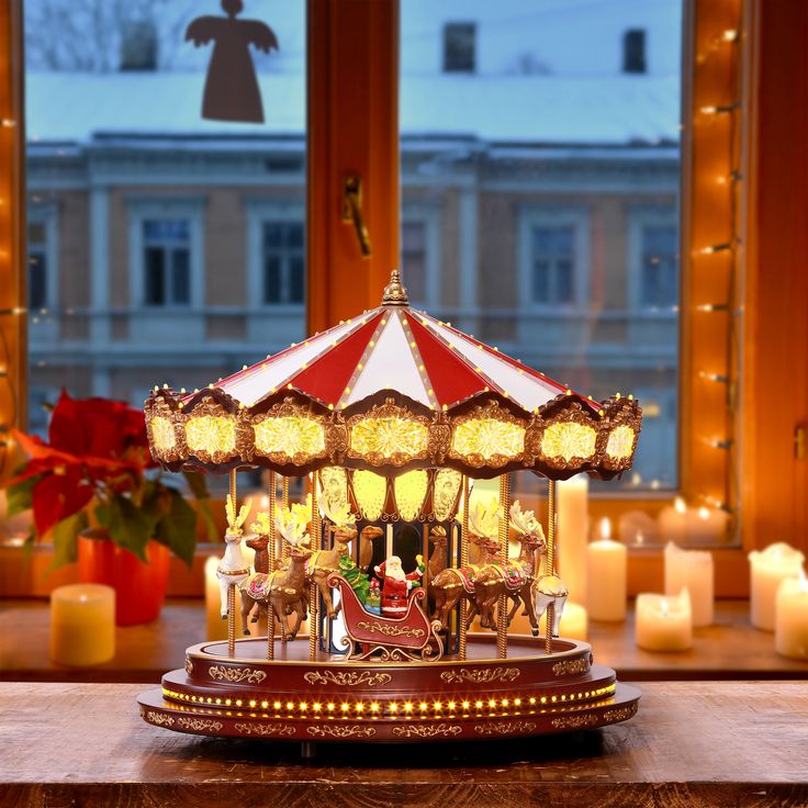 a merry go round with lit candles in front of a window and christmas decorations on the windowsill