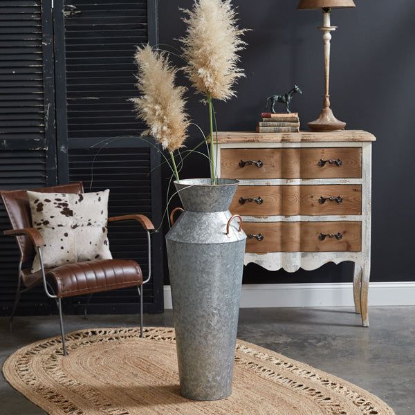 a vase with some flowers in it sitting on a rug next to a chair and dresser