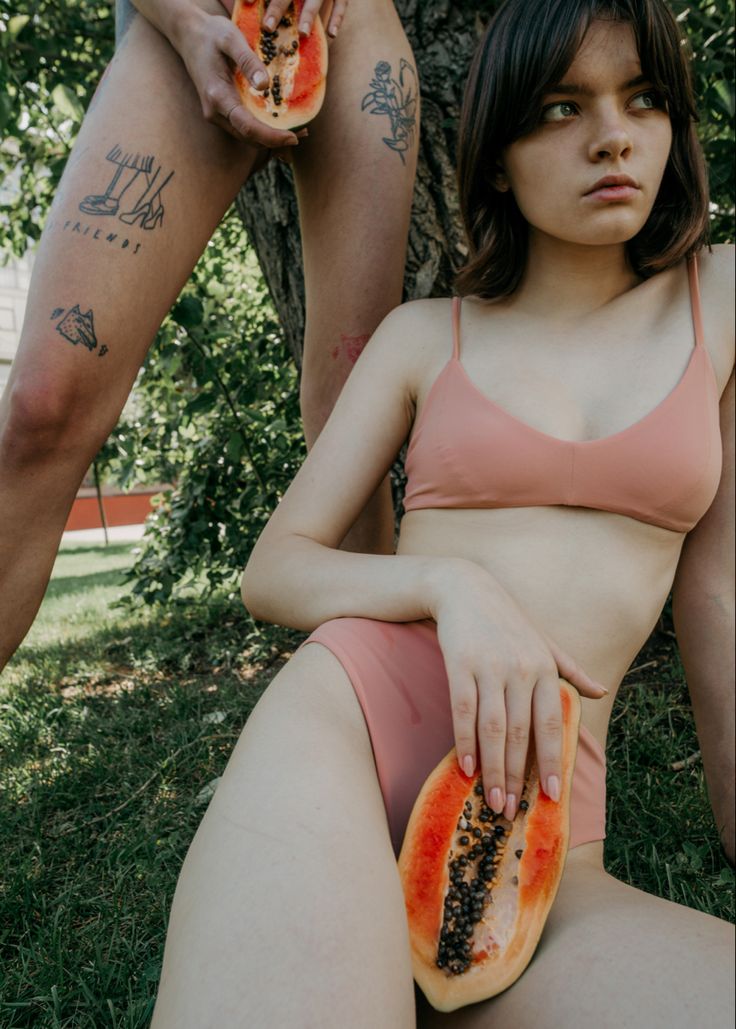 a woman sitting in the grass with a piece of fruit next to her legs and arm