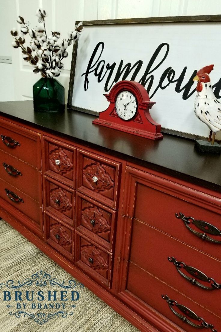 a red dresser with an old fashioned clock and rooster figurines on it's top