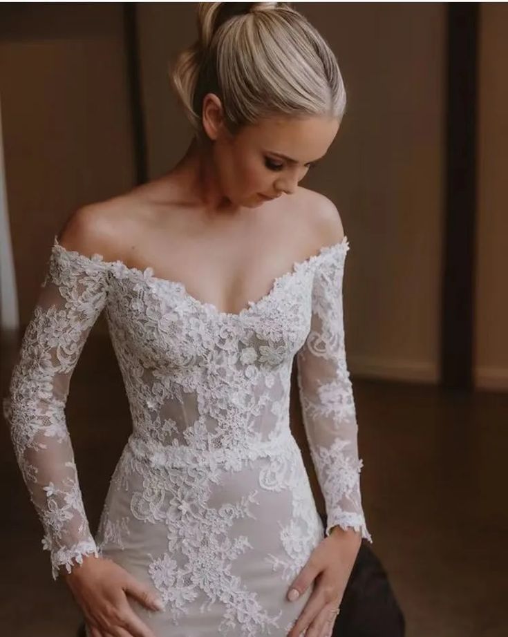 a woman in a white wedding dress with long sleeves and lace on her arms, looking down