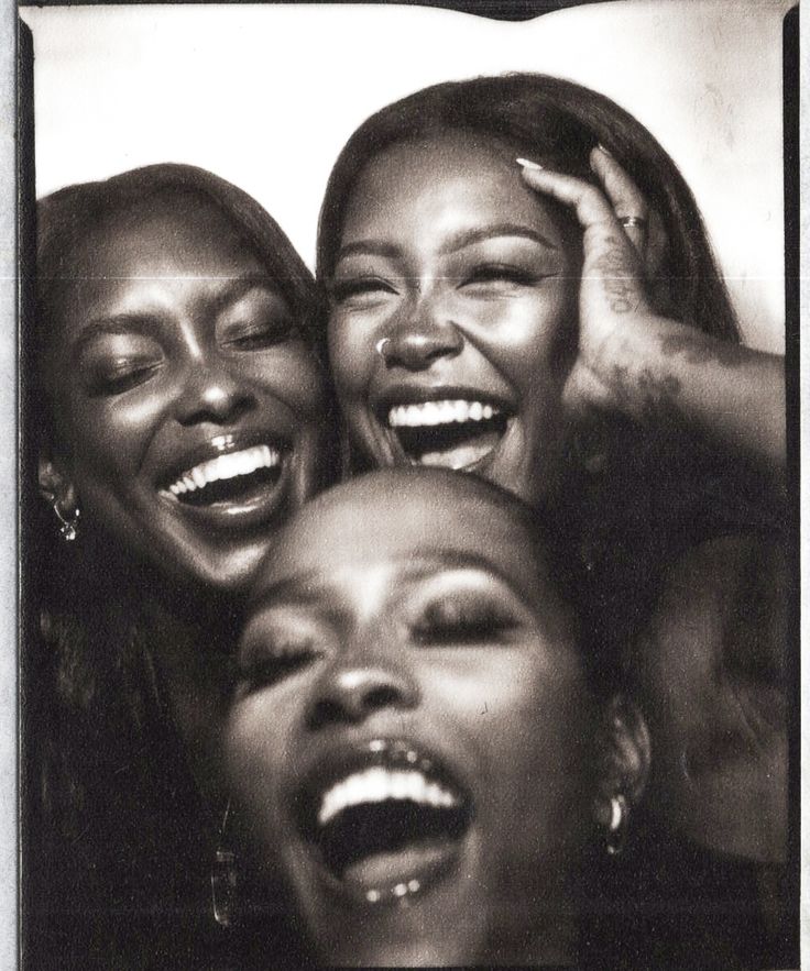 three women laughing together with their mouths open and one holding her head in the other's hands