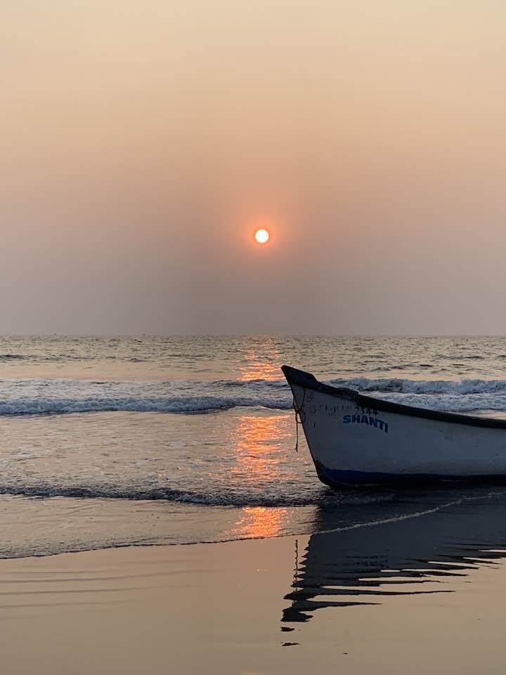 a small boat sitting on top of a beach near the ocean under a setting sun