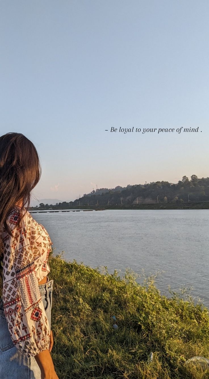 a woman standing on top of a lush green field next to a lake with a quote above her head