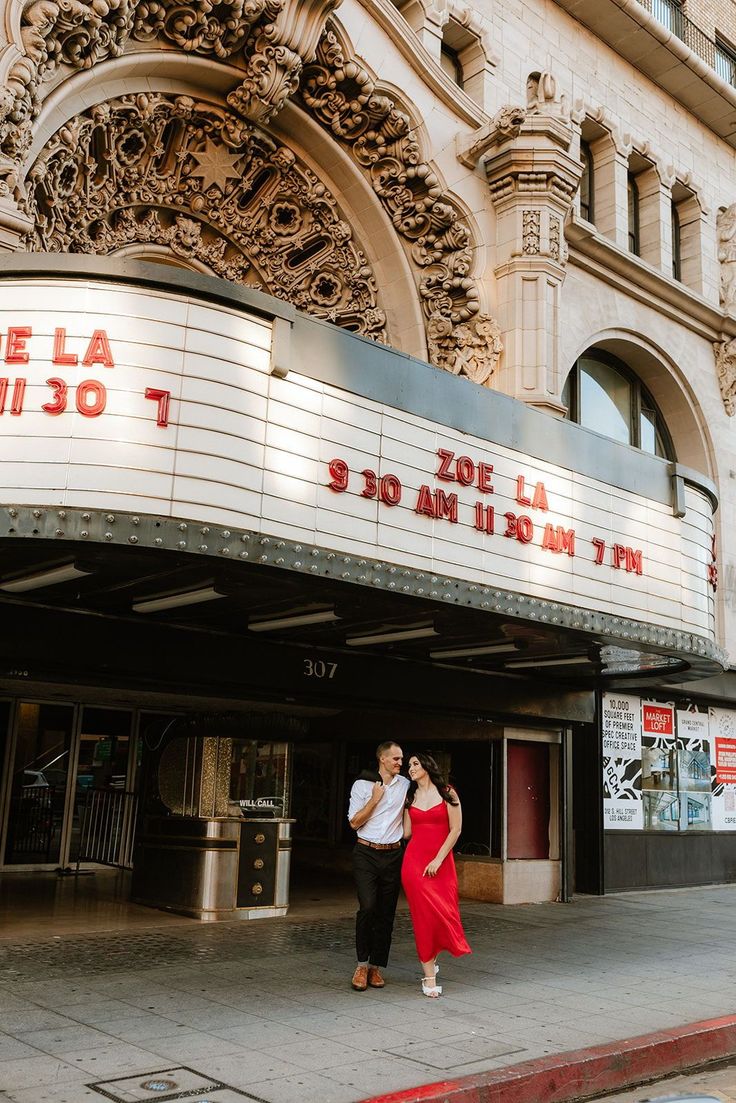 a man and woman standing in front of a theater marquee on the street