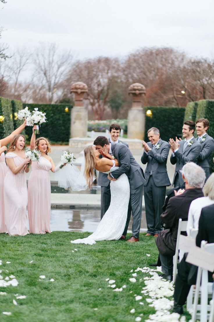 a bride and groom kiss as they walk down the aisle at their wedding in front of an elegant garden