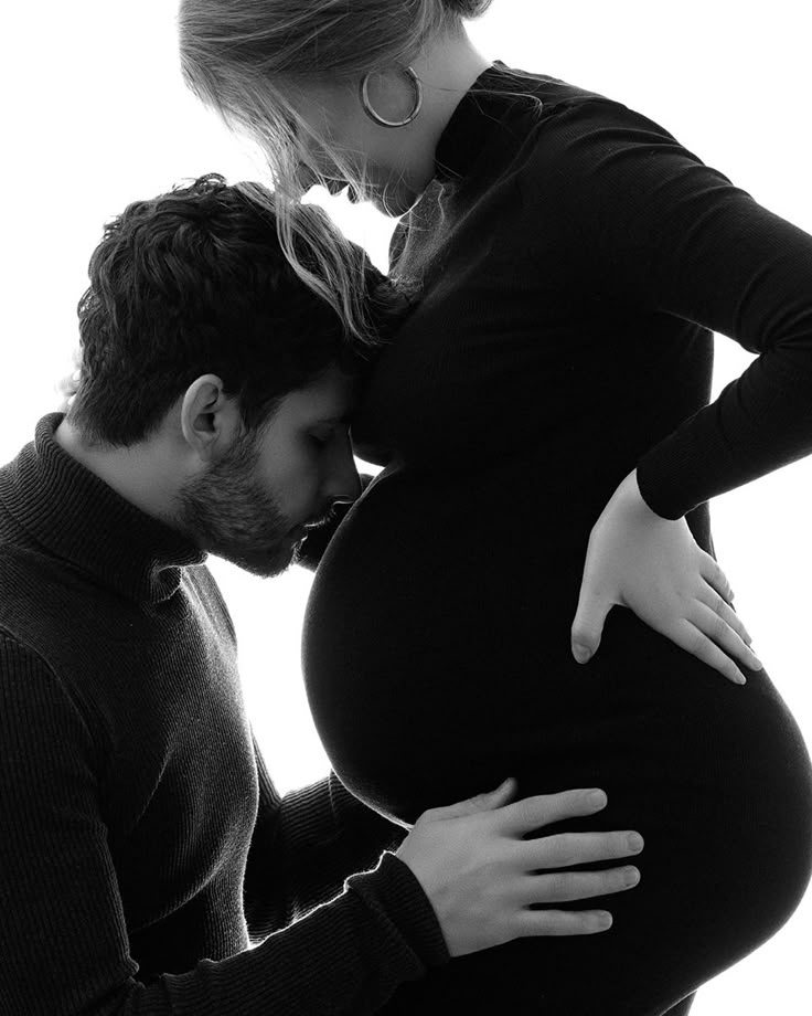 a pregnant couple kissing each other while the woman is holding her belly up to her stomach