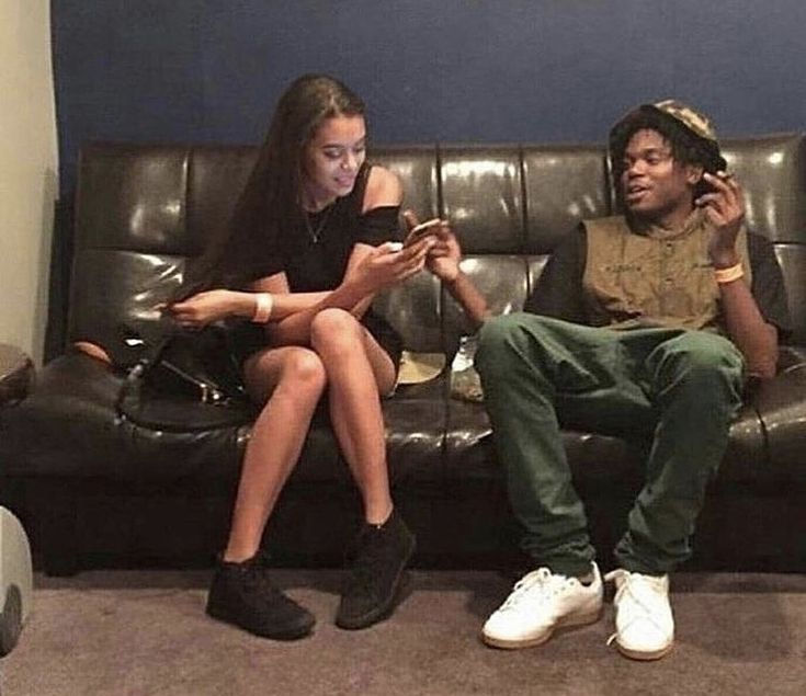 two people sitting on a couch looking at their cell phones while one person holds a phone up to his ear