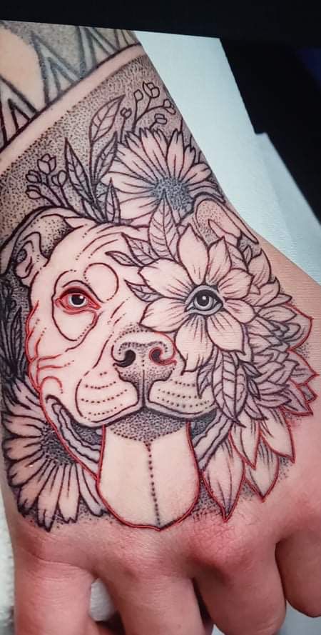 a hand with a dog's face on it and flowers around the wrist tattoo