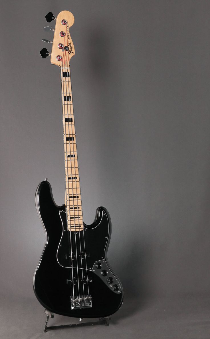 an electric bass guitar sitting on top of a stand in front of a gray background