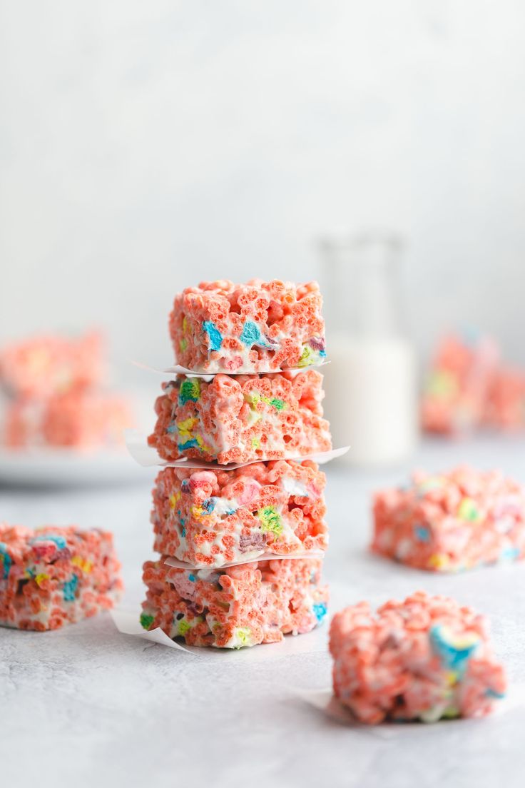 sprinkled rice krispy treats stacked on top of each other with milk in the background