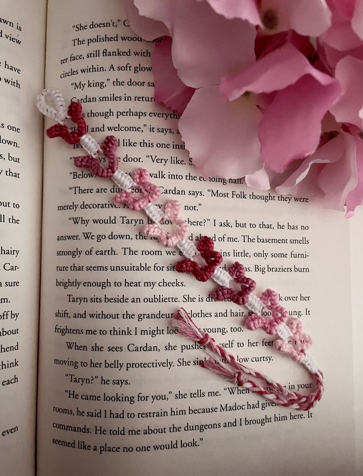 a crocheted bookmark laying on top of an open book next to pink flowers