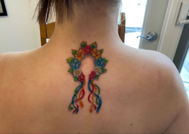 a woman with a tattoo on her back that has a colorful ribbon and flowers in it