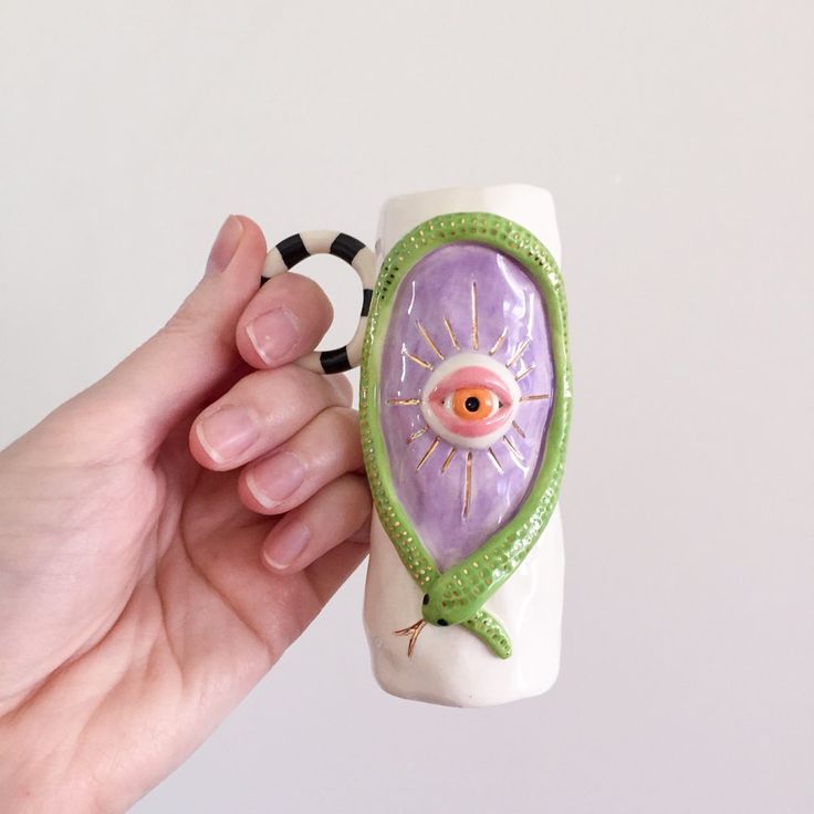 a hand holding a ceramic mug with an eye on it