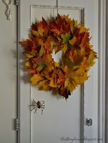 a wreath is hanging on the front door with autumn leaves and a spider in it