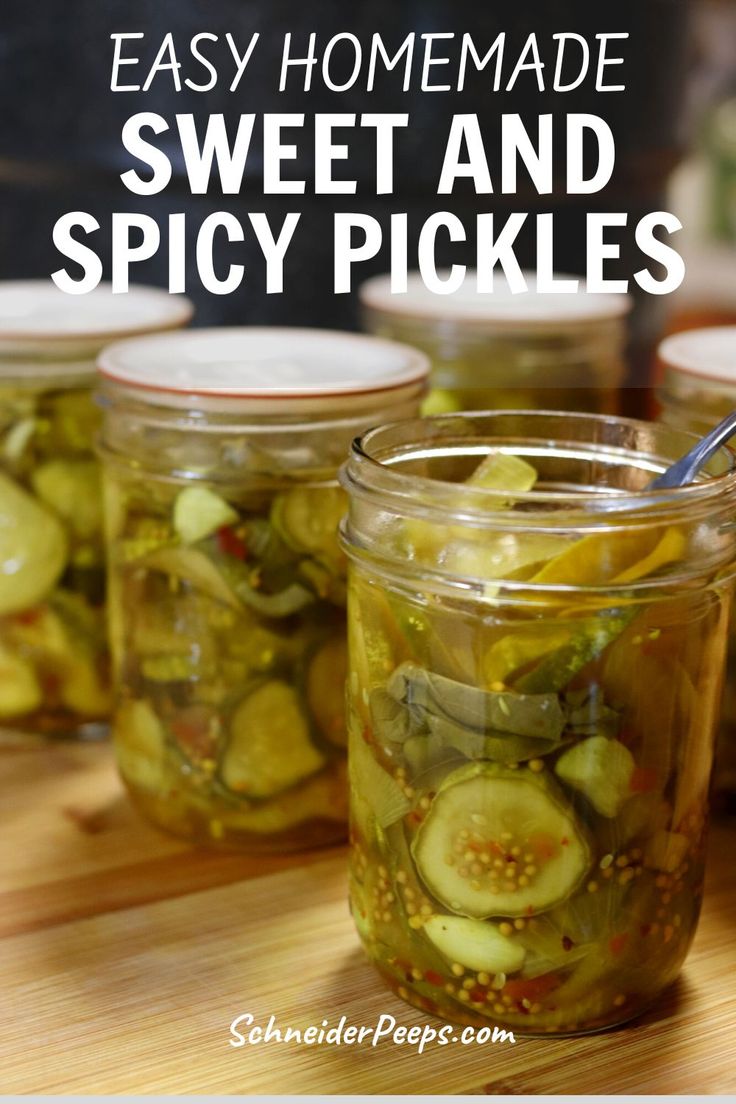 jars filled with pickles sitting on top of a wooden table next to a spoon