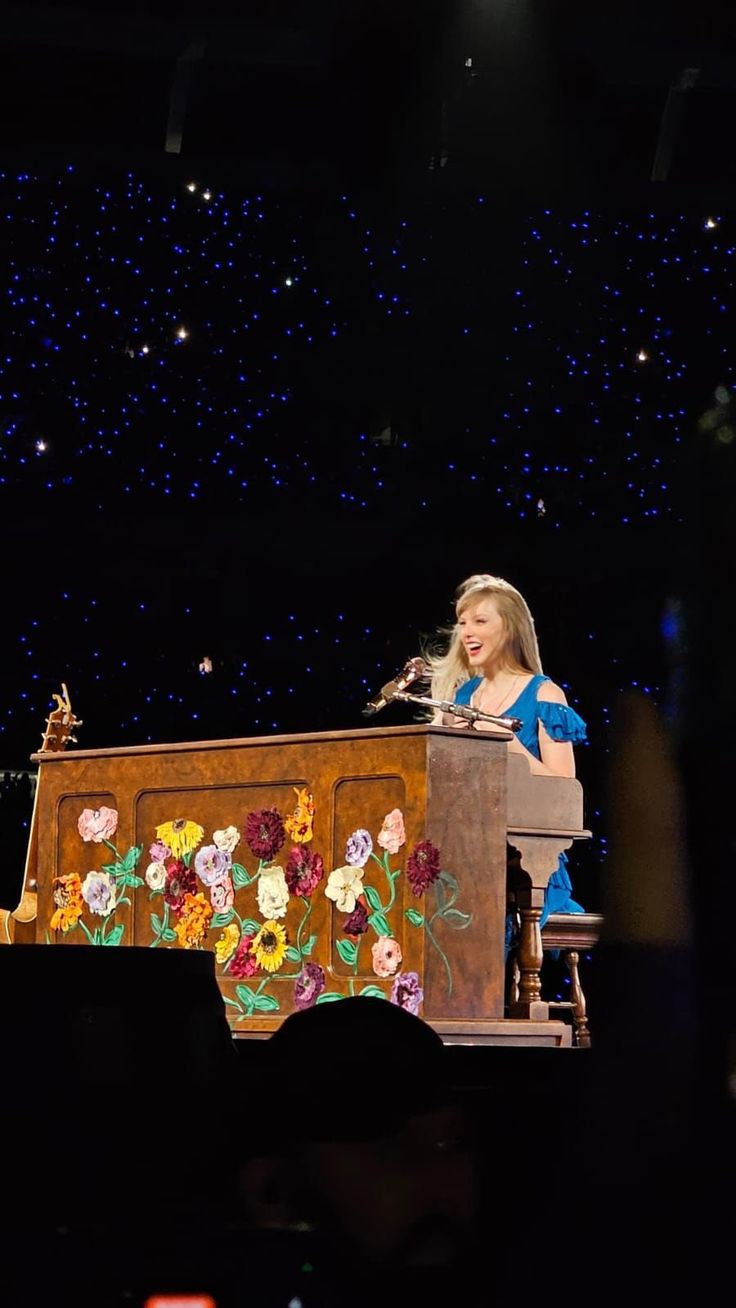 a woman standing at a podium on top of a stage with flowers painted on it