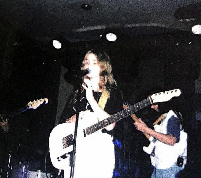 two people are singing and playing guitars in a dark room with lights on the ceiling