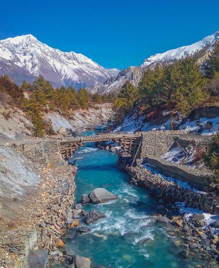 a river running through a valley surrounded by snow covered mountains in the middle of winter