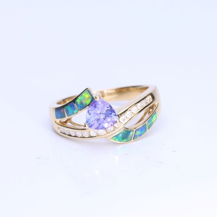 Wear the CIRARI 14K Yellow Gold Inlay Opal Trillion Tanzanite Ring to exude elegance. This ring is incredibly well-made and has a striking trillion-cut tanzanite set in a gorgeous inlay of opals. The design, set in dazzling 14K yellow gold, skillfully combines classic charm with contemporary refinement. This CIRARI masterpiece, a monument to timeless beauty and tasteful design, will elevate your look. Give yourself over to the allure of this magnificent ring. Fine Jewelry Tanzanite Rings With Diamond Cut, Trillion Cut Tanzanite Rings For Wedding, Fine Jewelry Multi-stone Trillion Cut Ring, Fine Jewelry Opal Ring With Multi-stone For Anniversary, Gold Trillion Cut Gemstone Ring, 14k Gold Jewelry With Trillion Cut Accent Stones, Trillion Cut Multi-stone Rings As Gift, Gold Tanzanite Birthstone Ring For Anniversary, Trillion Cut 14k Gold Rings For Anniversary