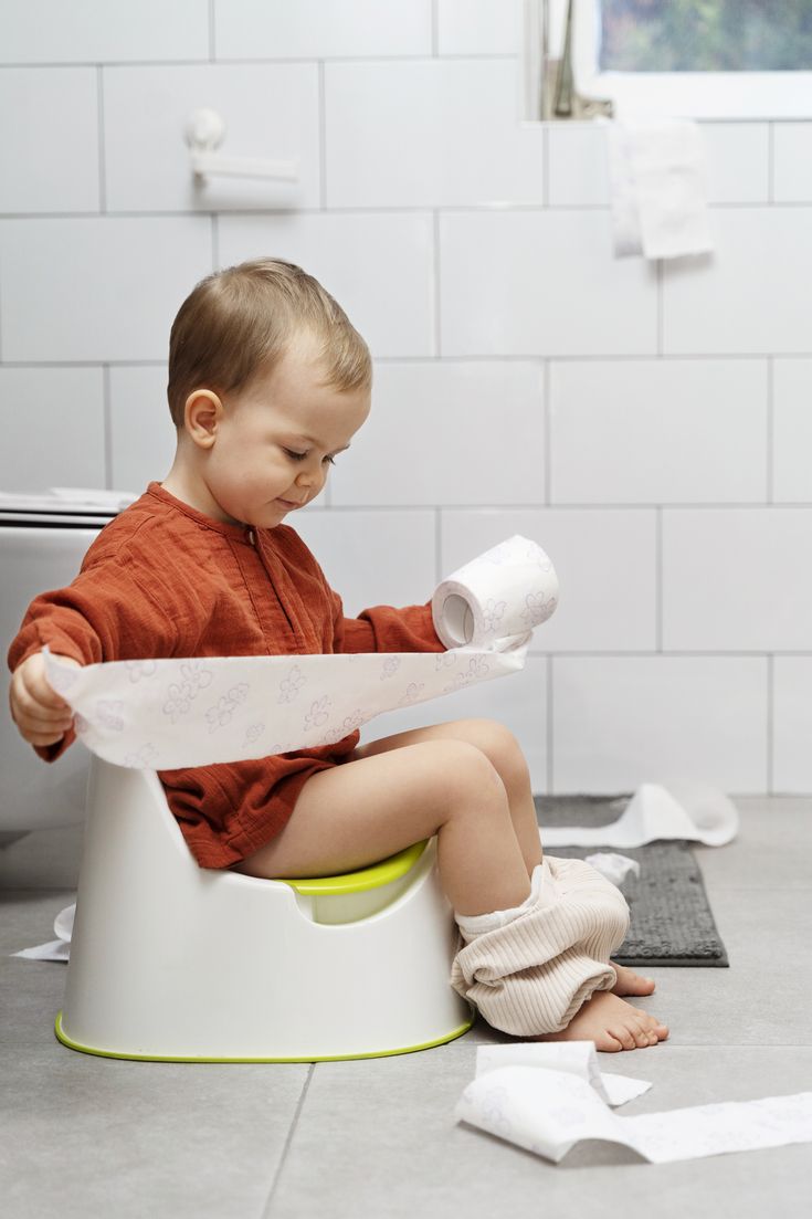 a little boy sitting on top of a potty with toilet paper in his hands