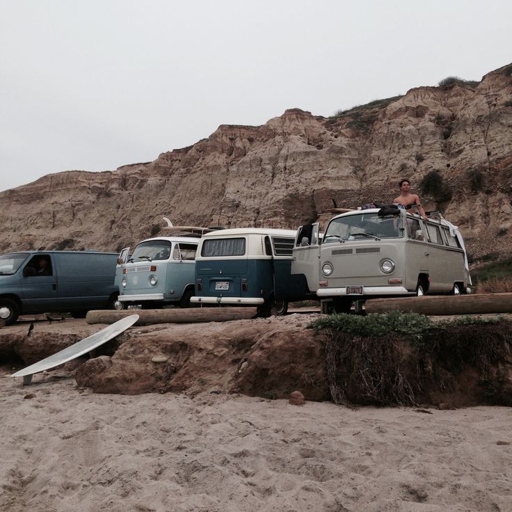 an old vw bus is parked on the beach next to other cars and surfboards