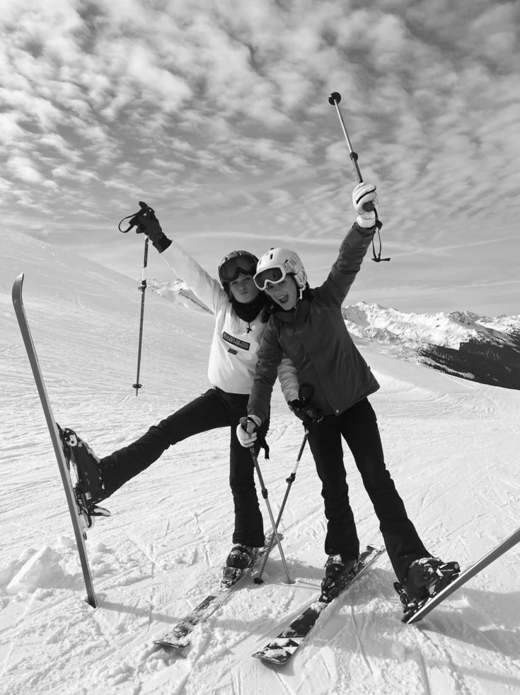 two people standing on top of a snow covered slope with skis and poles in their hands