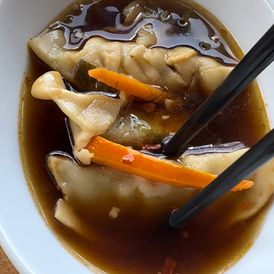 a bowl filled with dumplings and carrots next to chopsticks on a table