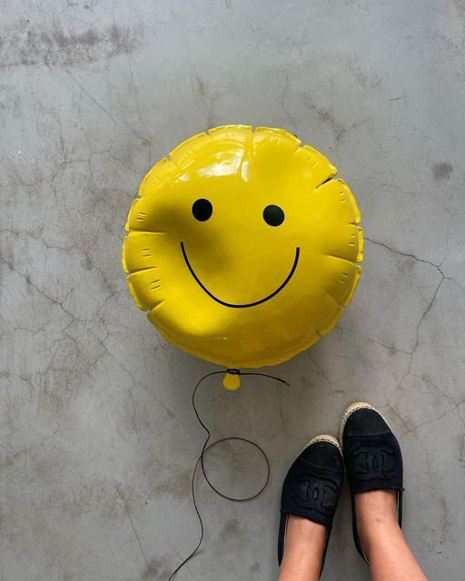 a yellow smiley face pillow sitting on the floor next to a pair of black shoes